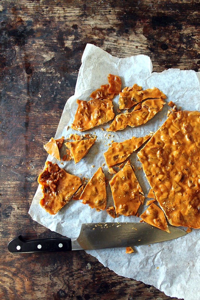 Shards of ginger pecan brittle recipe being cut on baking paper. 