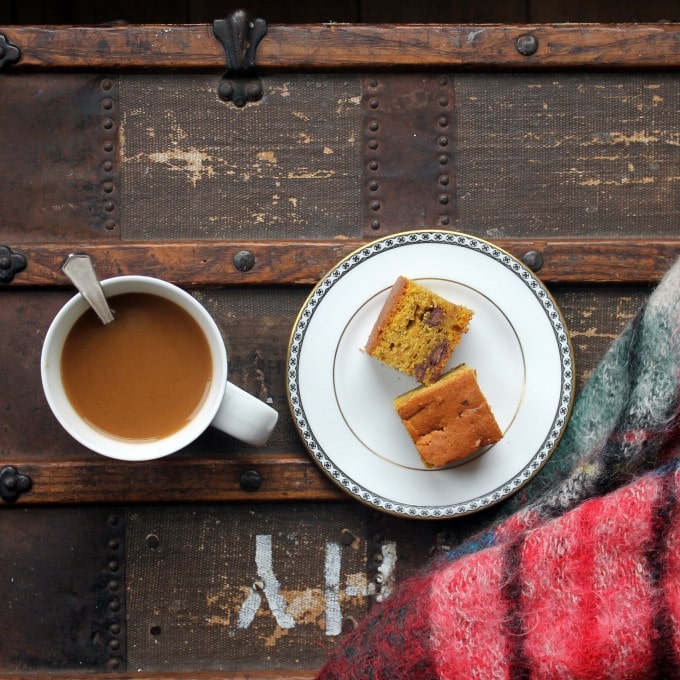 A plate of cake sitting on top of a wooden table, with a mug of tea.