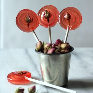 Close up of lollipops sticking out of a metal cup with rose buds.