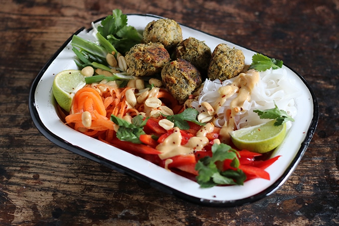 Close up of an enamel dish full of noodles, falafel balls and vegetables.