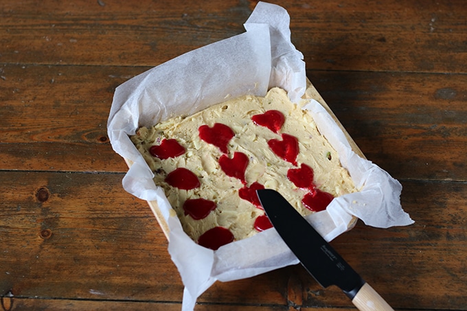 Blondie batter with spoonfuls of raspberry sauce being formed into heart shapes.