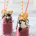 Mugs of smoothie topped with cream, cookies and straws.
