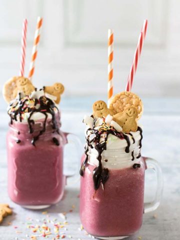 Mugs of smoothie topped with cream, cookies and straws.