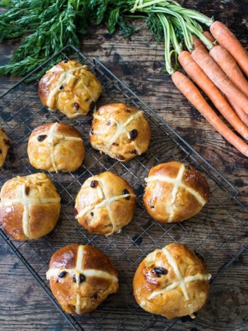 Wire rack of hot cross buns next to a bunch of carrots.