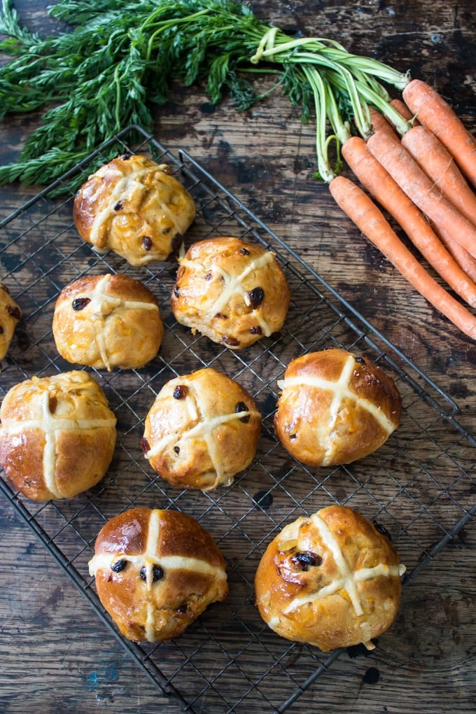 Wire rack of hot cross buns next to a bunch of carrots.