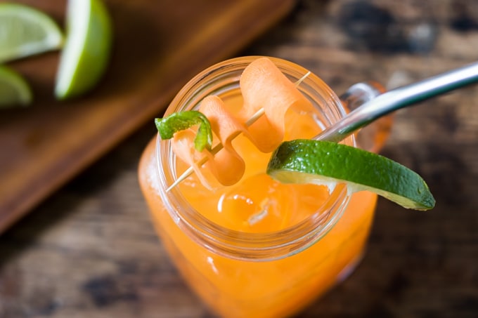 Overhead shot of a glass of carrot Moscow Mule cocktail, with a twist of lime and a peeling of carrot wound onto a toothpick.