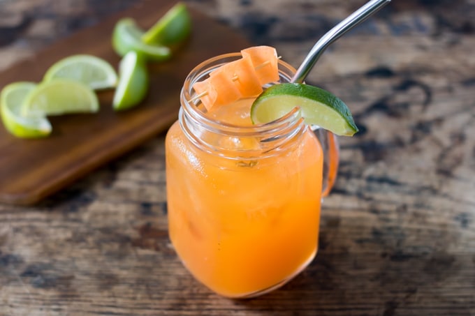 Glass of cocktail with a straw and lime wedge.