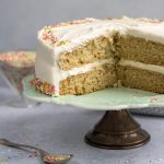 Vegan vanilla layer cake on a cake stand with slices removed.