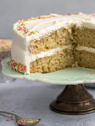 Vegan vanilla layer cake on a cake stand with slices removed.