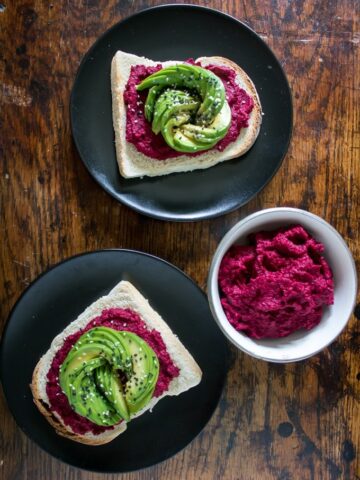 A table with plates of toast topped with hummus and avocado.