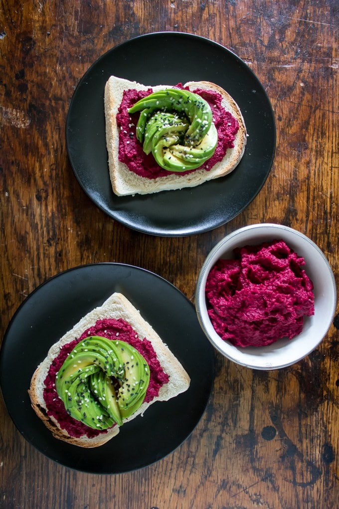 A table with plates of toast topped with hummus and avocado.