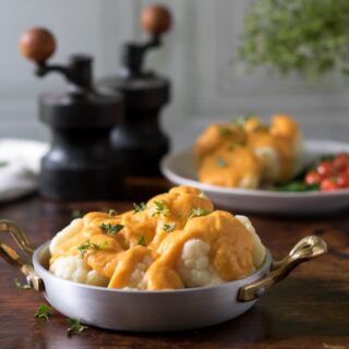 A dish of cauliflower cheese on a wooden table.