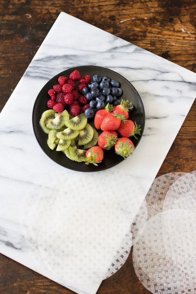 Fruit on a plate next to dry summer roll rice papers ready to make fruit summer rolls with vanilla yogurt dip