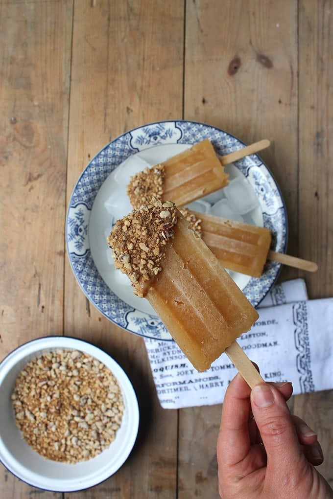 Hand holding an Apple Popsicle with Date Caramel Crumble and chopped pecans. 