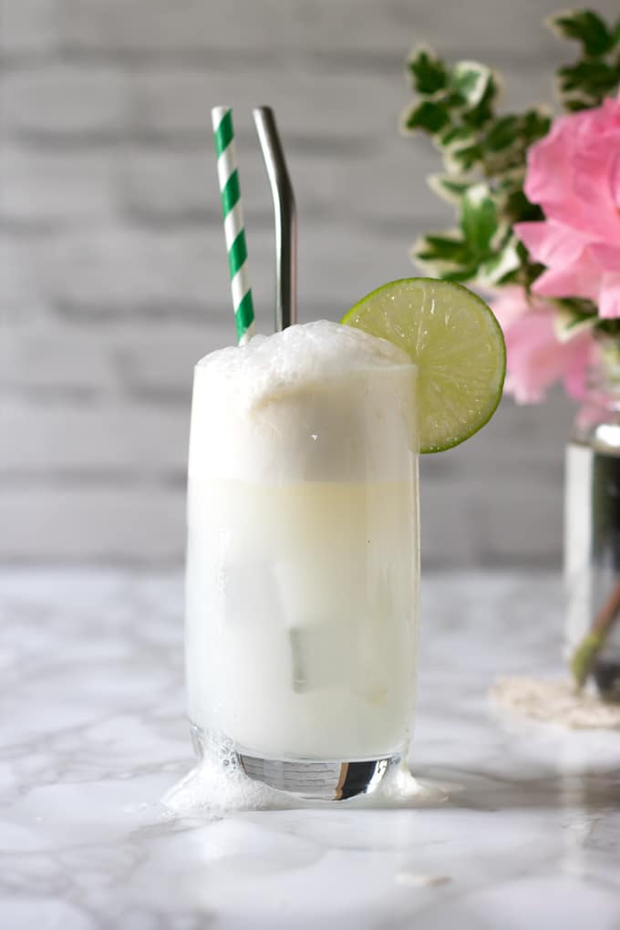 Gin and Tonic Float overflowing in a tall glass with straws and a slice of lime. 