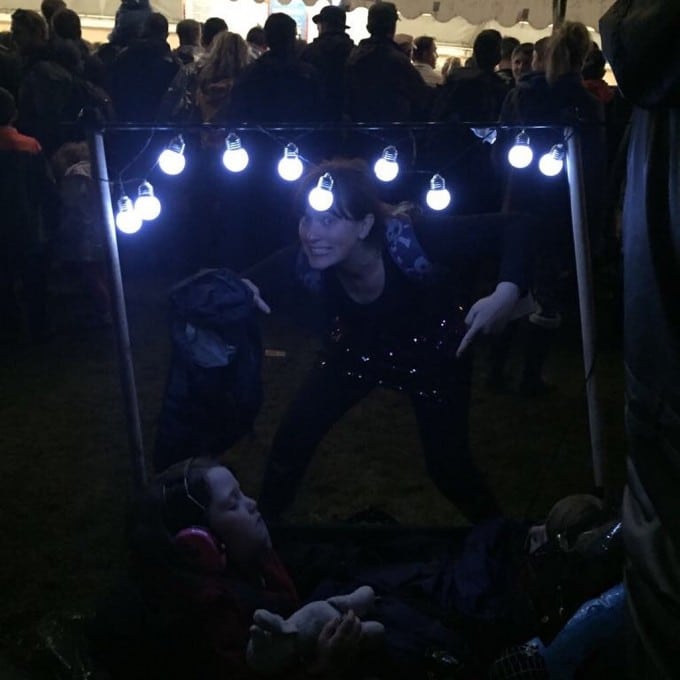 People dancing at night at a festival with a child asleep in a trolley.