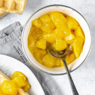 A bowl of mango compote (made with fresh or frozen mango) next to a waffle with the zingy compote.