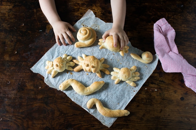 Child's hand picking up a bread roll shaped like a spider.