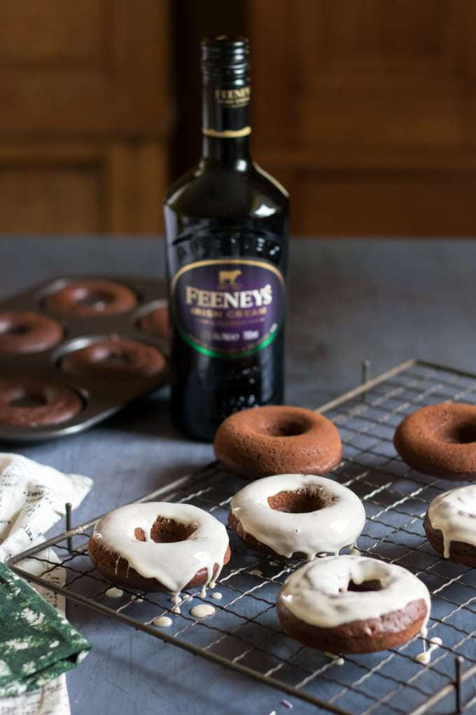 Glazed baked donuts on a wire rack in front of a bottle of Irish Cream. 
