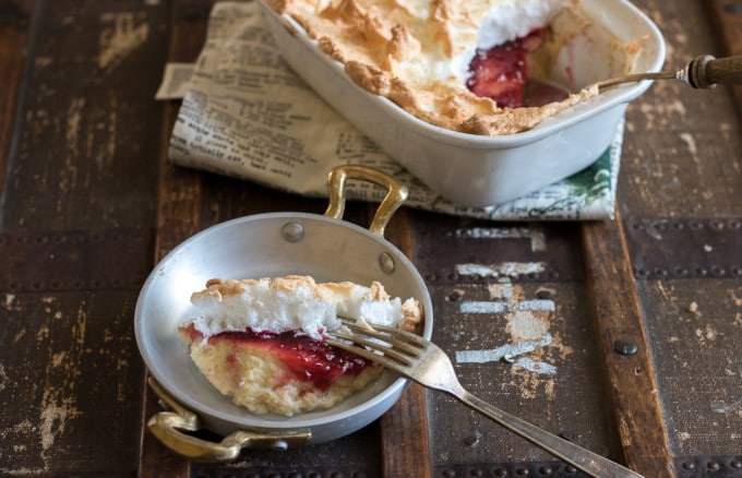 A bowl of custard with jam and meringue, with a baking dish of Queen of Puddings in the background.
