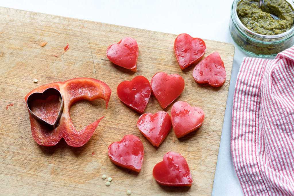 Red peppers being cut into heart shapes with a cookie cutter to be used on puff pastry tartlets. 