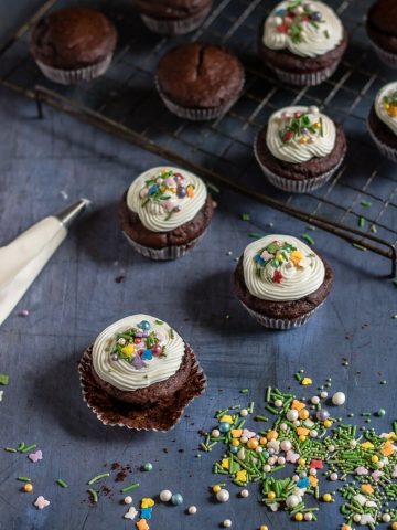 Easy vegan chocolate cupcakes with white icing and colourful sprinkles on a cooling rack