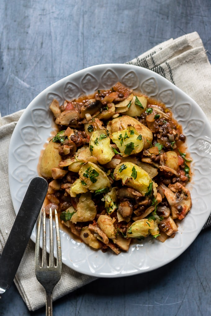 Vegan shepherd's pie with crushed new potatoes on a plate with parsley. Gluten free and full of lentils and mushrooms. 