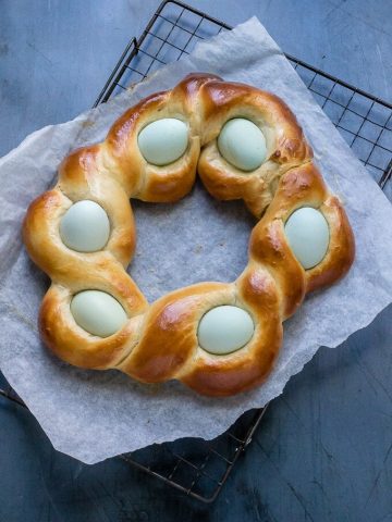 Easy Italian Braided Easter Bread cooling on a rack, with pale blue eggs nestled in the ropes of the braids.