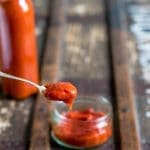 A spoonful of thick tasty homemade tomato ketchup with a bottle of it in the background.