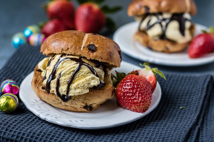 A close up of a hot cross bun with ice cream and strawberries.