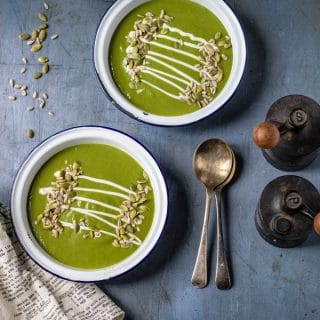 Two bowls of kale soup served with seeds and a drizzle of cream, on a table with vintage spoons and salt and pepper shakers.