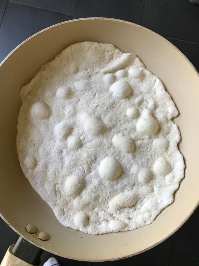 Naan in a frying pan with bubbles appearing.