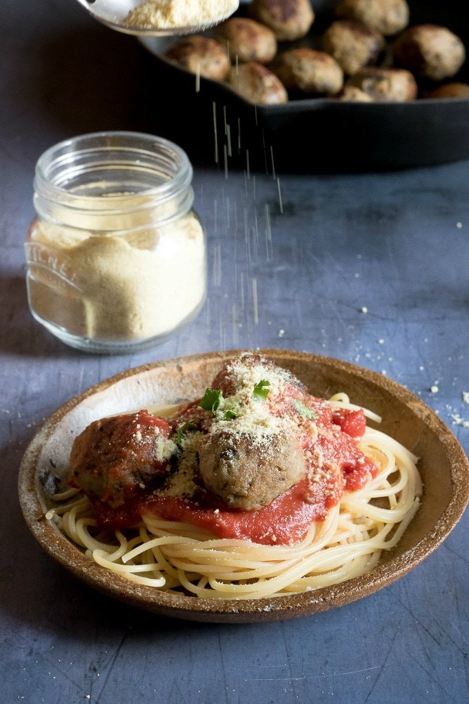 Easy cheesy vegan parmesan cheese being sprinkled on spaghetti and aubergine meatballs with tomato sauce