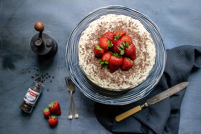 Overhead shot of easy one-bowl chocolate cake with vanilla black pepper buttercream, topped with shaved dark chocolate and fresh strawberries