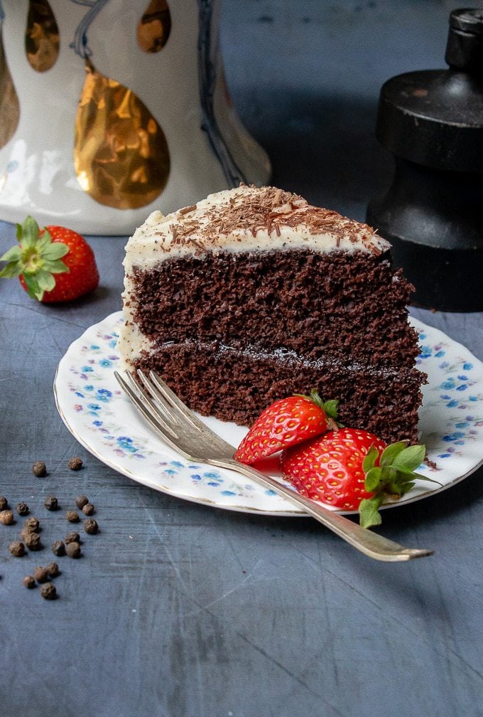 Close up of a slice of fluffy and moist one-bowl chocolate cake with a vanilla black pepper buttercream and fresh strawberries