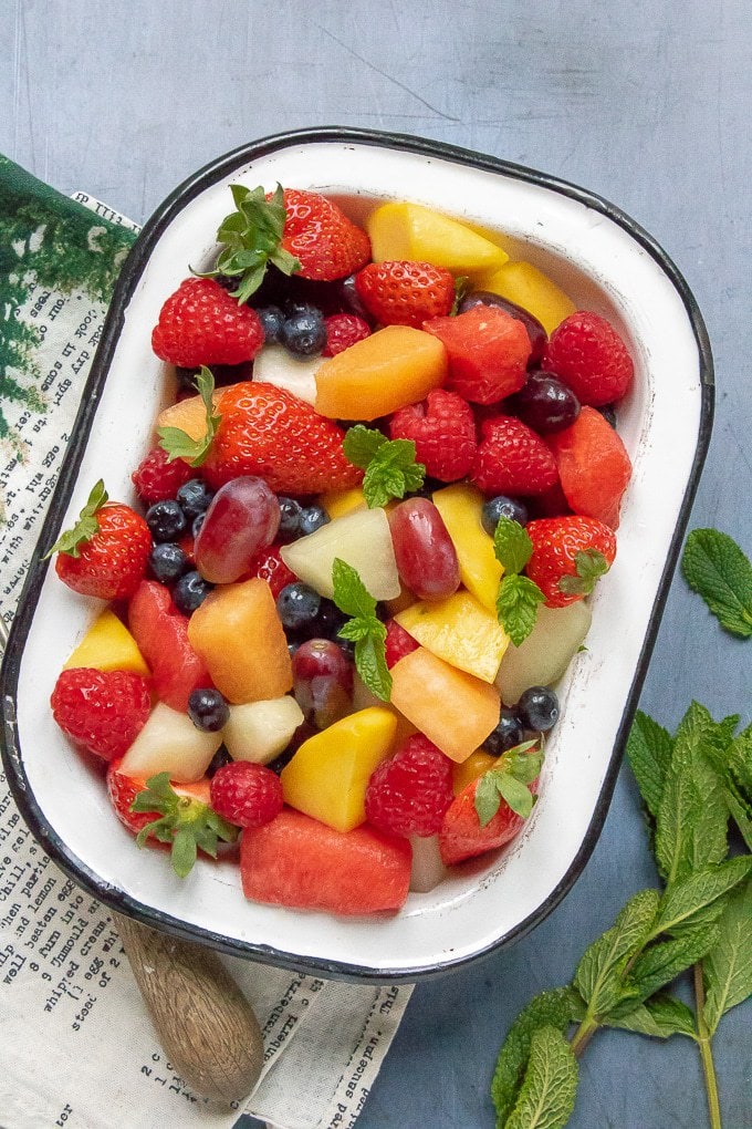 Close up of a bowl of fruit salad, with berries, grapes, melon, mango and sprigs of mint. 