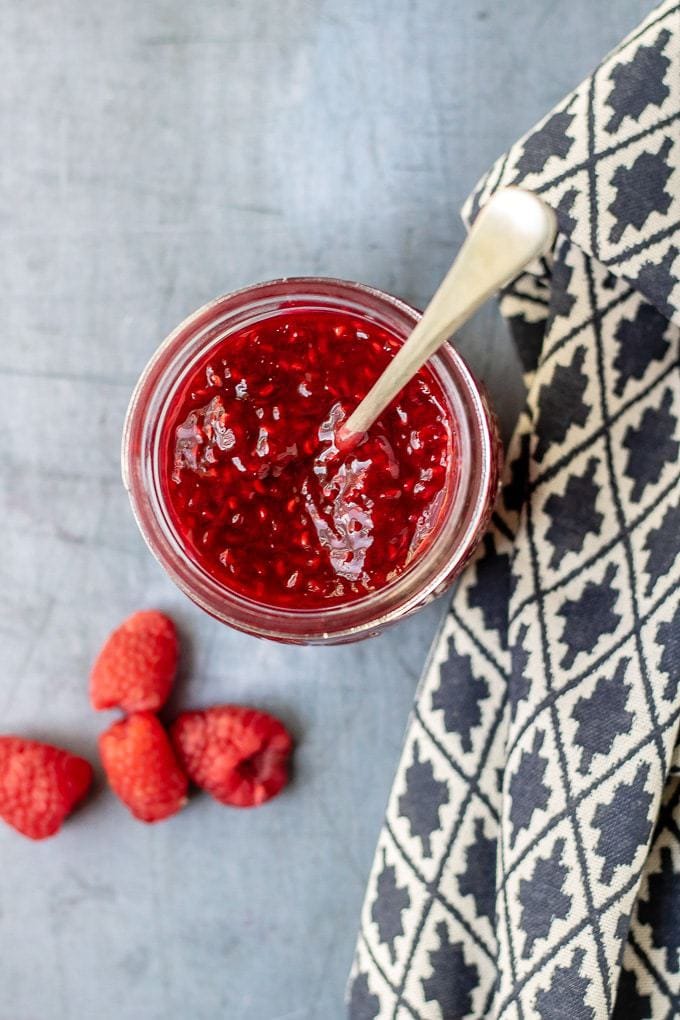A jar of raspberry compote with a spoon in it.