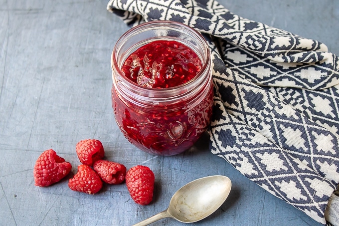 Jar of compote with raspberries next to it.