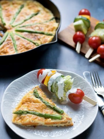 A slice of sweet potato frittata with asparagus on a plate with salad on a stick.