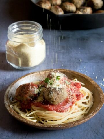 A plate of spaghetti with tomato sauce and (aubergine) eggplant meatballs and vegan parmesan cheese sprinkled on top.