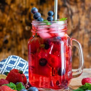 A glass of berry iced tea made with berry loose tea, ginger and berries. With berries on the table and sprigs of mint.