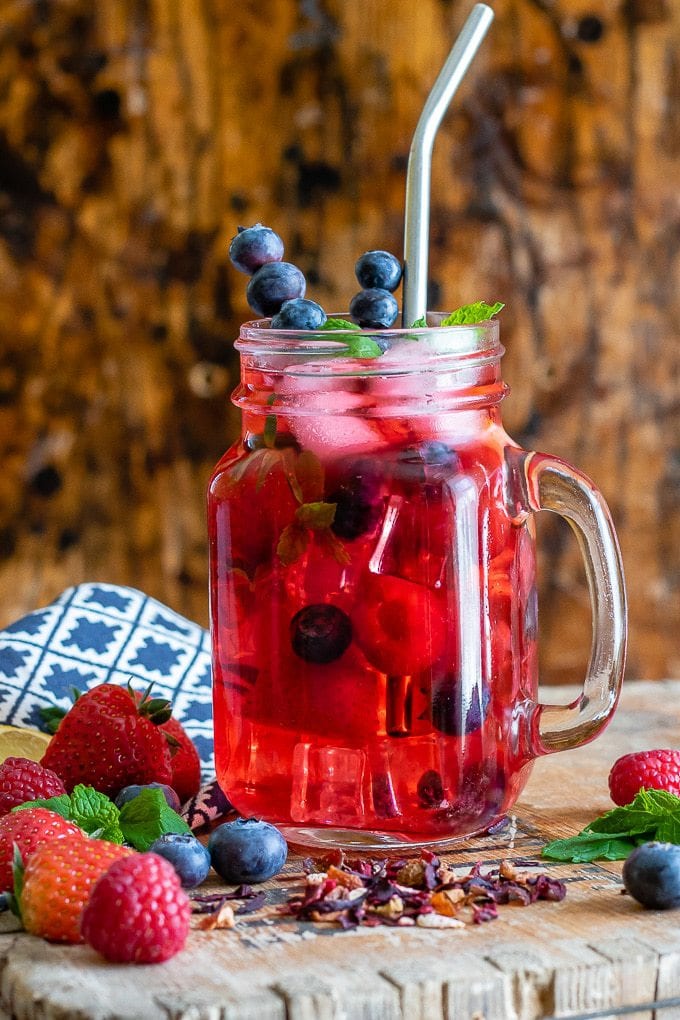 A glass of berry iced tea with berries on the table and sprigs of mint. 