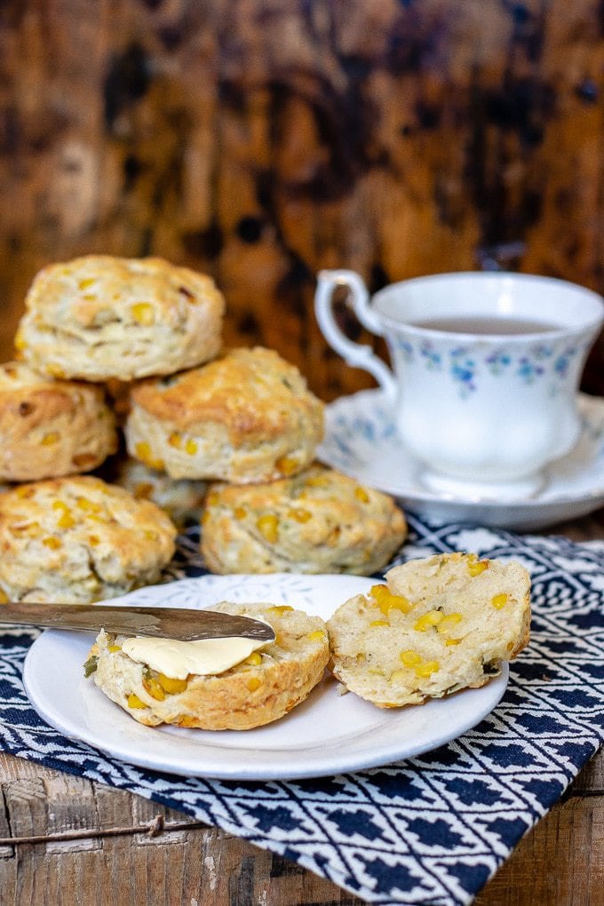 Spreading butter on sweet corn jalapeno scones on a plate with a vintage cup of tea