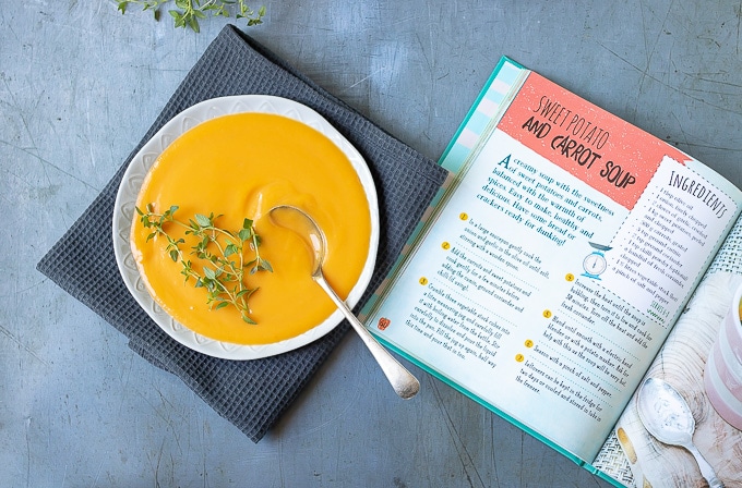 A bowl of carrot sweet potato soup next to the book Living on the Veg - a kids guide to vegetarianism, 