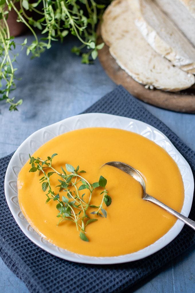 Close up of creamy carrot sweet potato soup in a bowl with fresh thyme