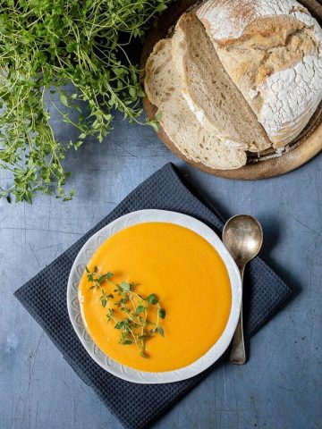 A bowl of quick, easy and creamy sweet potato soup with a vintage spoon, slices of sourdough bread and fresh thyme.