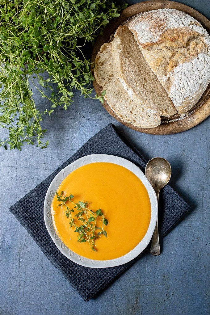 A bowl of quick, easy and creamy sweet potato soup with a vintage spoon, slices of sourdough bread and fresh thyme. 