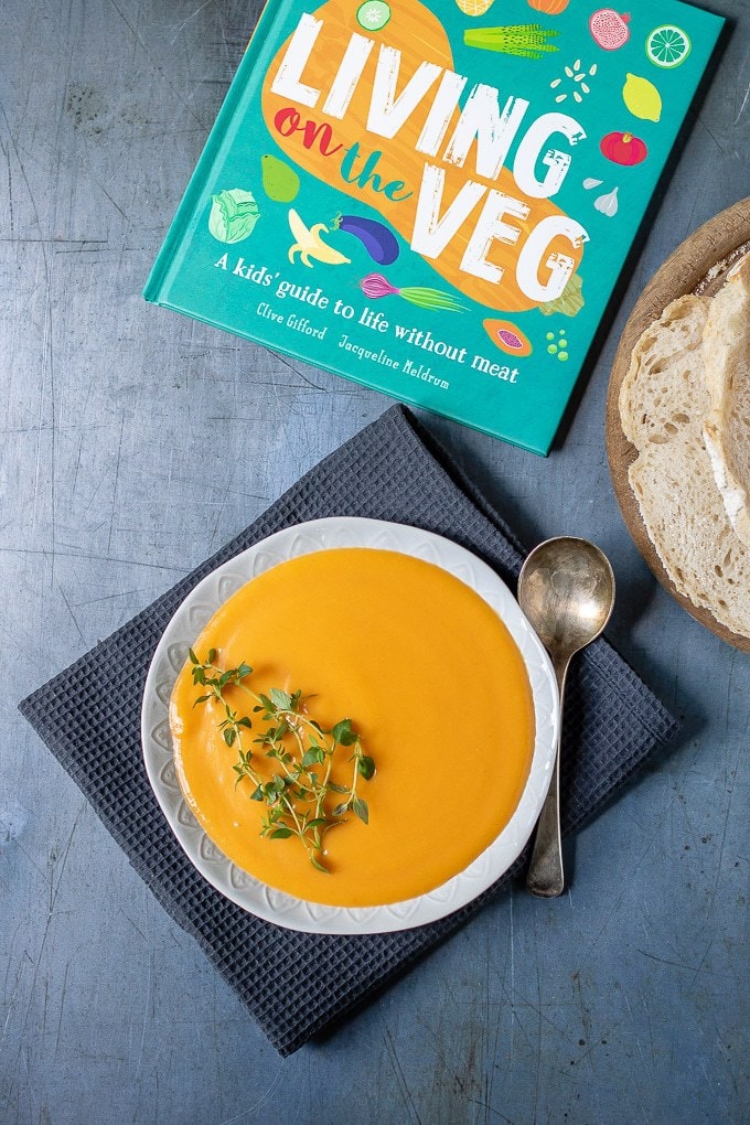 A bowl of creamy sweet potato soup next to slices of bread and the book: Living on the Veg
