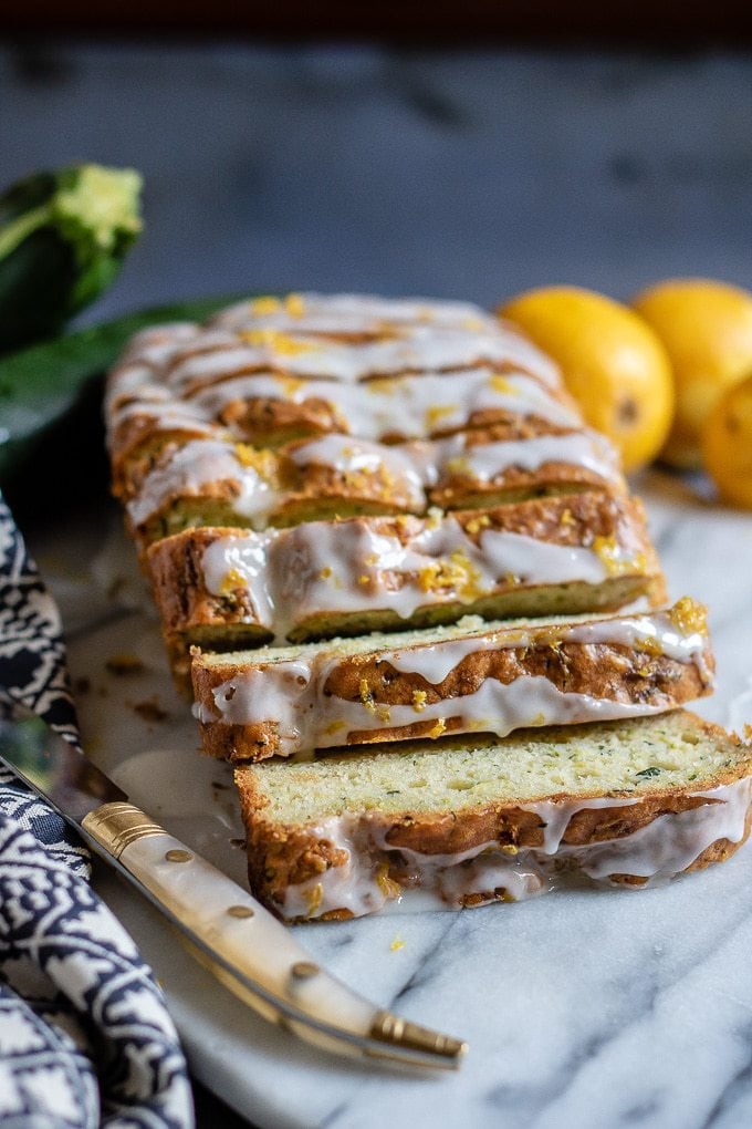 Sliced loaf of courgette cake topped with lemon drizzle.