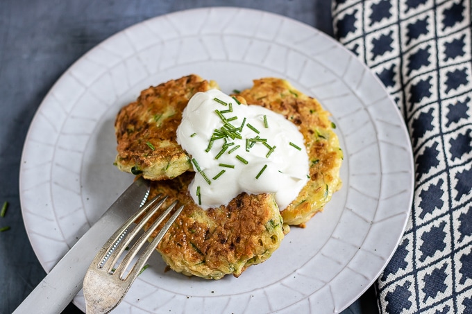 Cheesy courgette fritters recipe on a plate topped with sour cream and chopped chives.